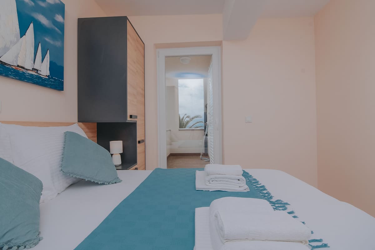 Habitación de hotel con cama, mesita de noche, un cuadro y vista a través de una puerta abierta.