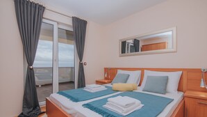Une chambre d’hôtel avec un grand lit, une table de chevet, une tête de lit en bois, un miroir et une vue sur la mer, accessible par une porte coulissante.