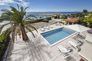 Un área de piscina con vista despejada al mar, una palmera y un suelo de baldosas.