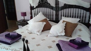 A neatly made bed with a floral-patterned bedspread, multiple pillows, and folded towels on a nightstand. - Casa dos Ventos (Olhao)