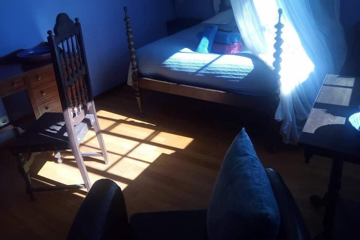 Ett sovrum med en säng i trä, en stol, ett skrivbord och ett fönster med gardiner.