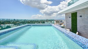 Une piscine à débordement située sur le toit, offrant une vue sur la ville, avec une balustrade en verre et une façade moderne.