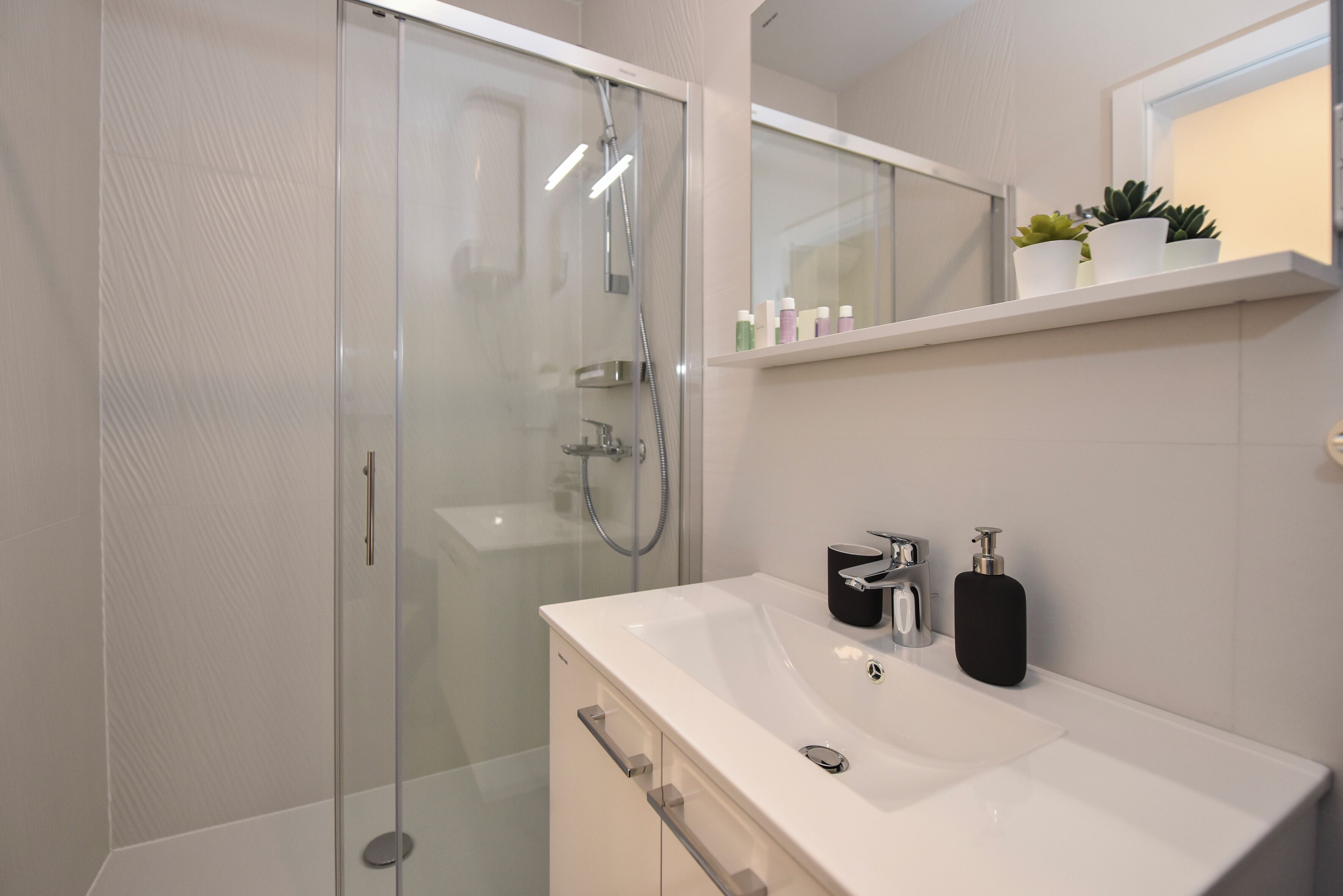 A modern bathroom with a glass-enclosed shower, a white sink, and a mirror above it.