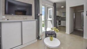 A modern living room with a flat-screen TV, a small round table with a vase, and a grey ottoman. - Pool Apartments & Rooms Mare (Novalja)