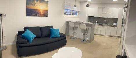 A modern living area with a sofa, a small table, a kitchen with white cabinets, and a bar area.