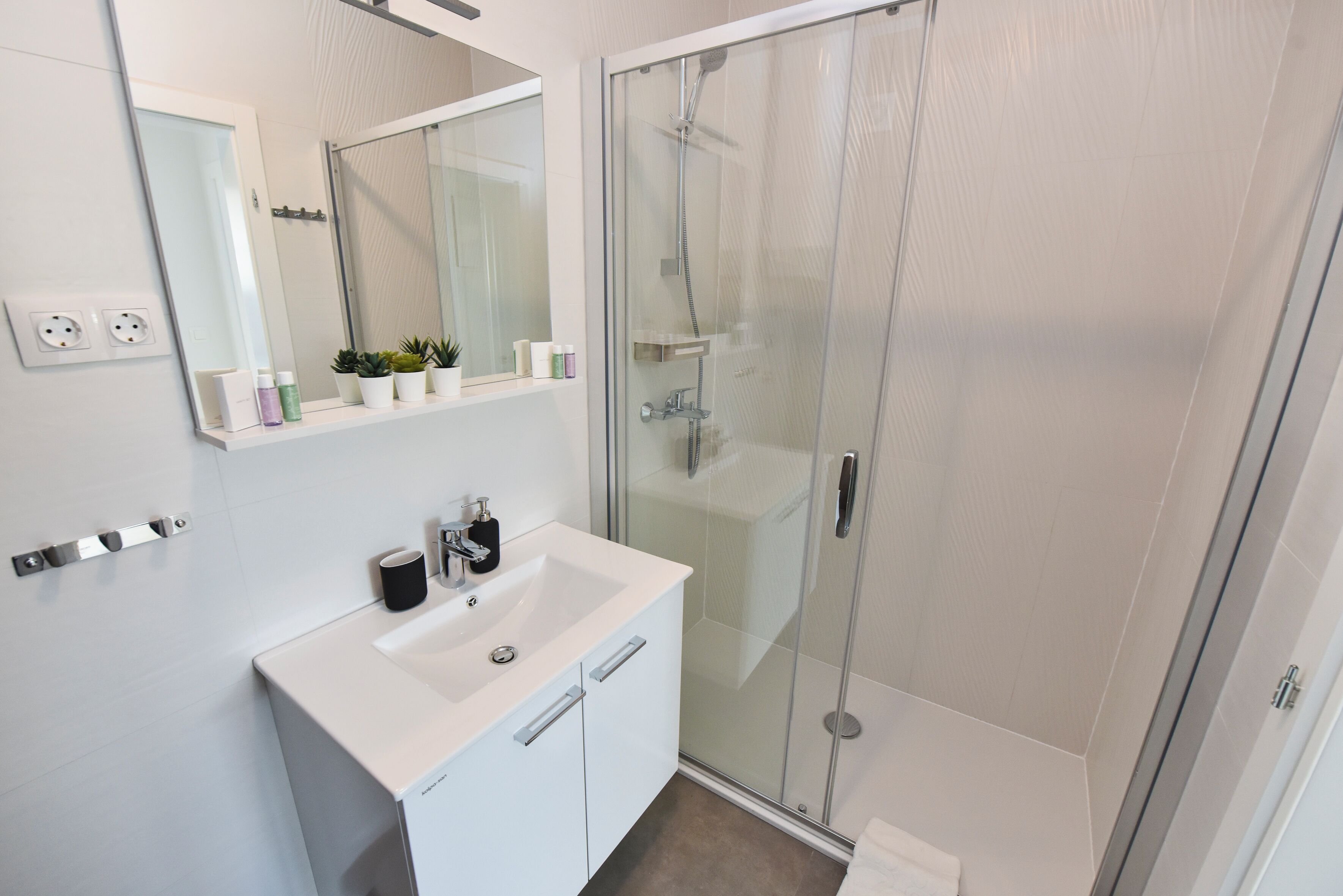 A modern bathroom with a white sink, mirror, and glass shower enclosure.