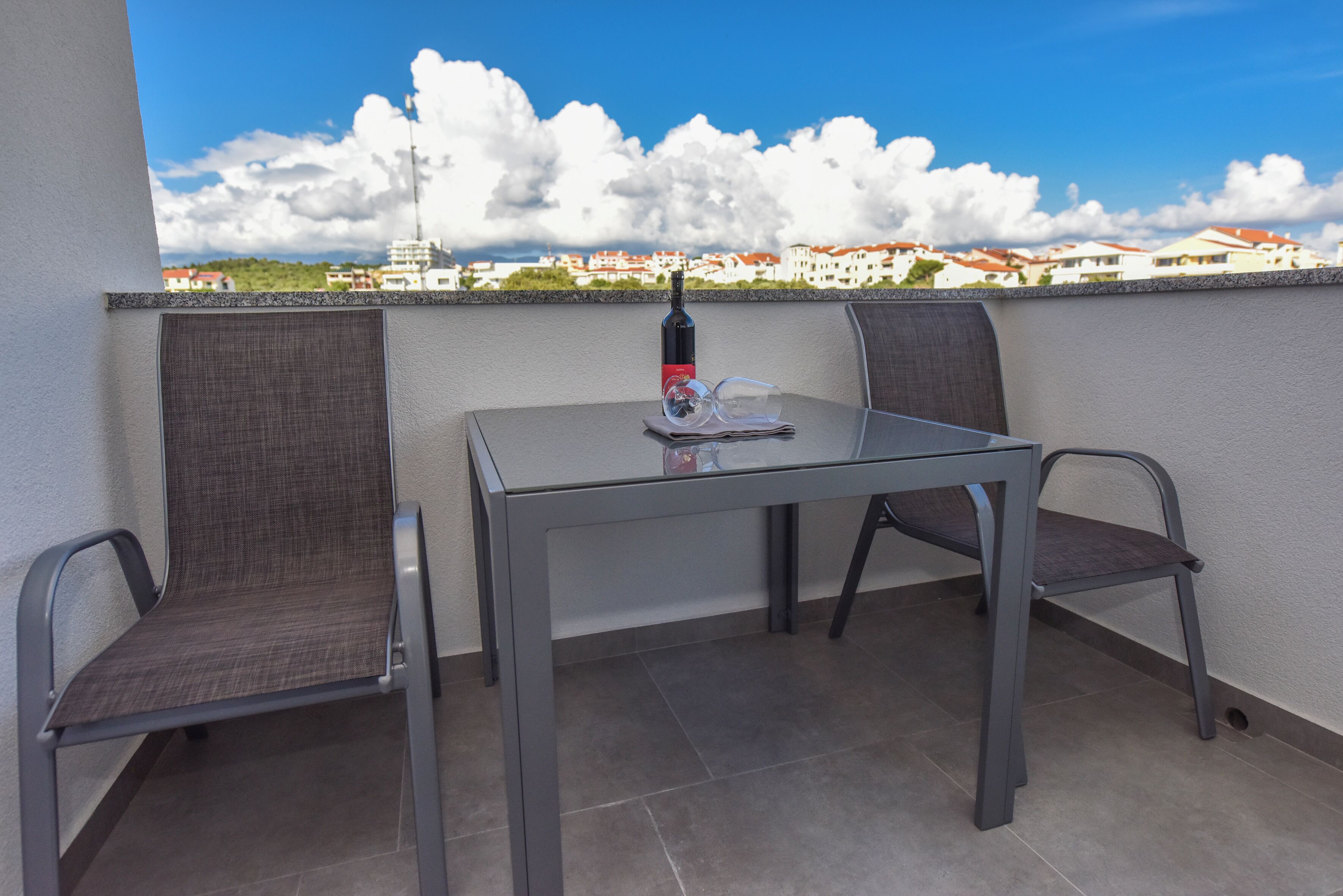 Un balcon avec une table et deux chaises, une bouteille et une paire de verres.