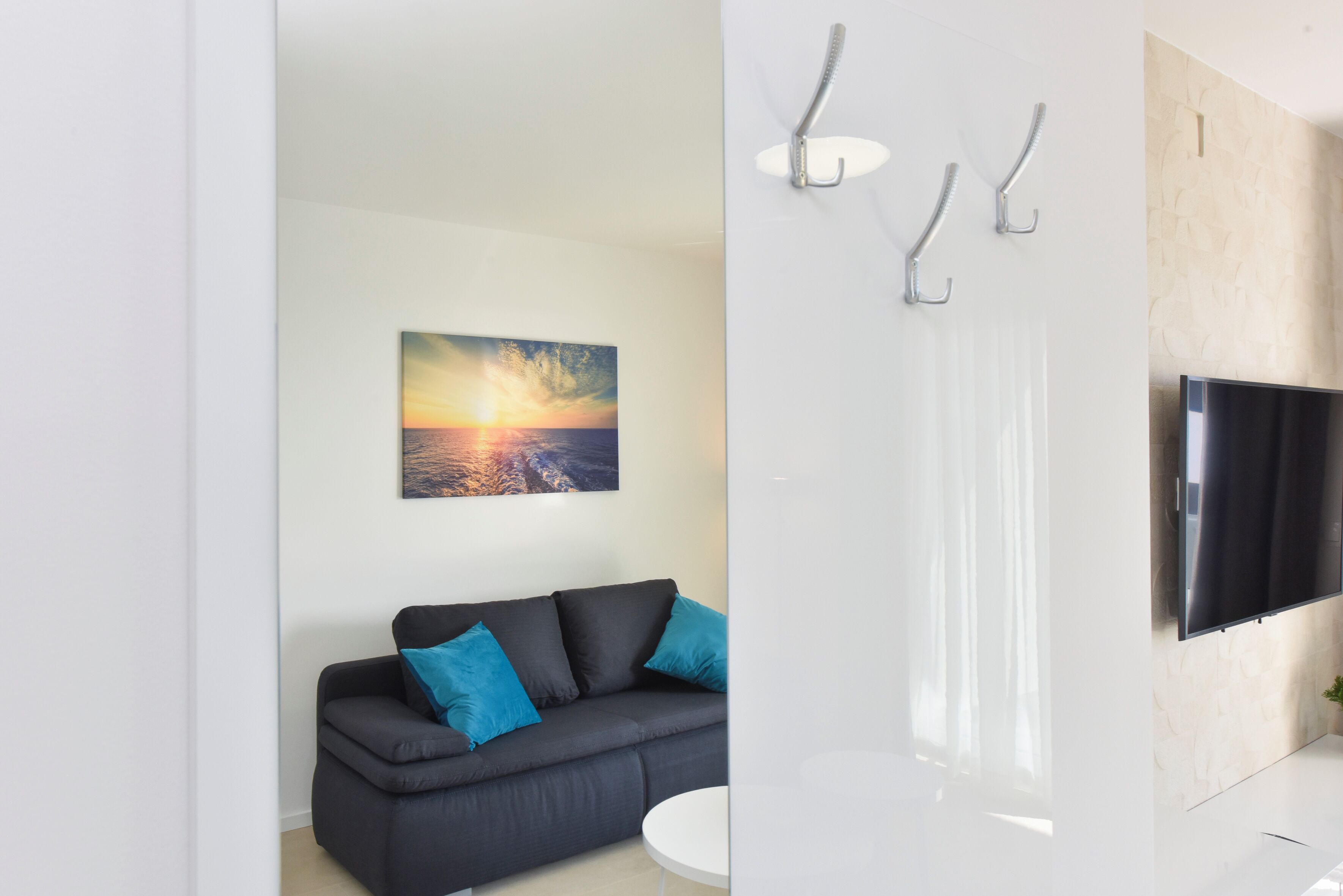 A modern living room with a black sofa, a white round table, and a painting of a sunset over water.