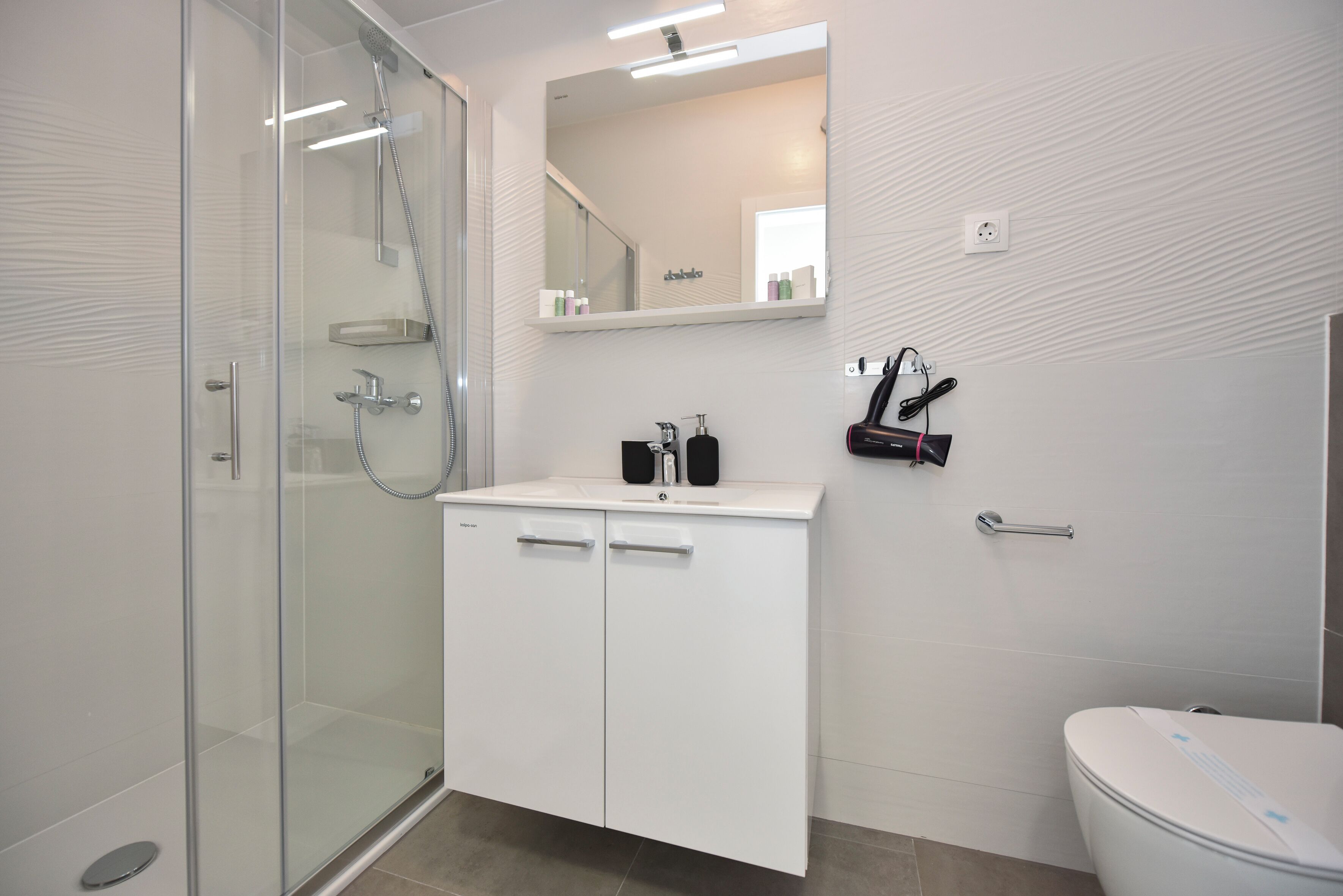 A modern bathroom with a glass shower enclosure, a white sink with a mirror above, and a toilet.