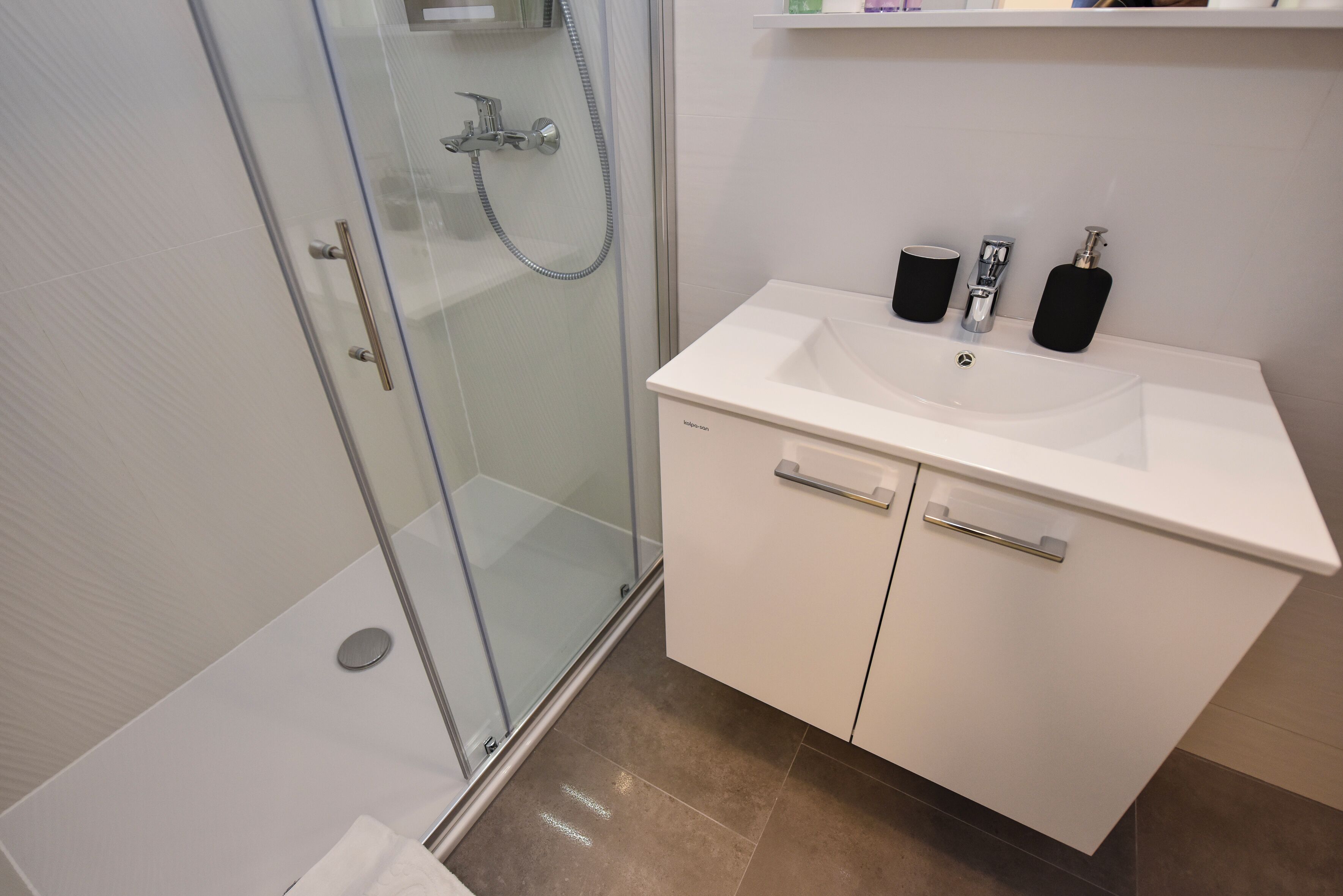 A modern bathroom with a glass shower enclosure, a white sink with a mirror, and a small shelf above the sink.