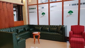 A green leather sofa, a small wooden side table, and a red chair in a room with a wooden wall and glass windows. - Sodere Resort Hotels Africa Union (Addis Ababa)