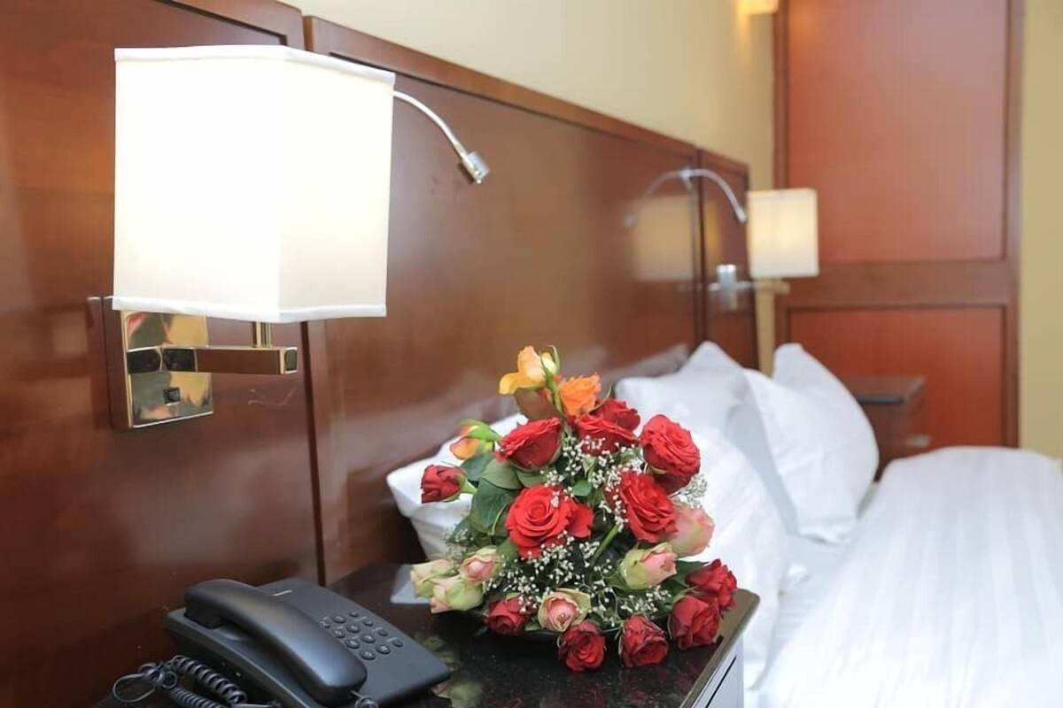 Ein Hotelzimmer mit einem Holzkopfteil, einem Nachttisch mit Telefon und Lampe sowie einem Strauß roter Rosen.
