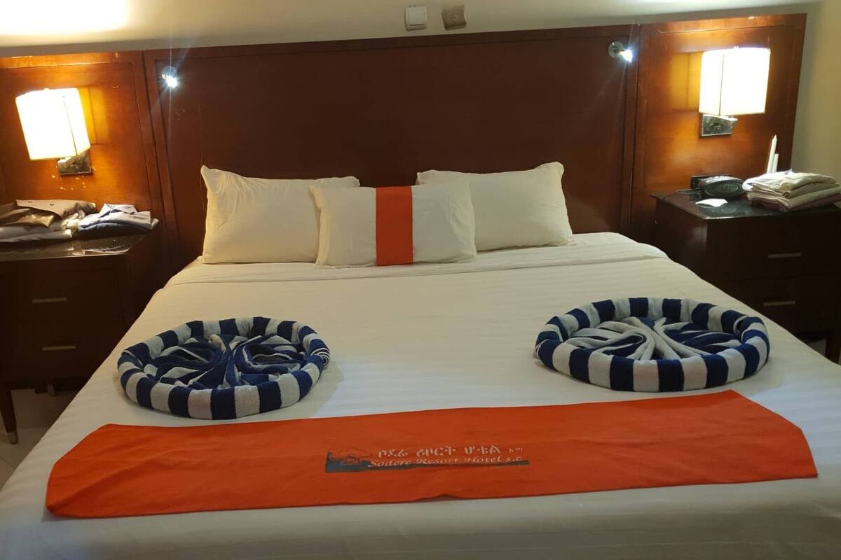 Ein Hotelzimmer mit einem großen Bett, zwei Nachttischen, einem Holz-Kopfteil und einem Beistelltisch mit Lampe.