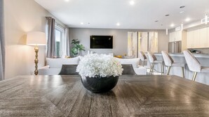 Zona pranzo moderna con tavolo in legno scuro, una ciotola nera con fiori bianchi e una cucina minimalista sullo sfondo.