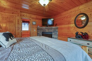 Ein Schlafzimmer in einer Holzhütte mit einem Bett, einem Kamin aus Stein, einem Fernseher und einer Kommode.