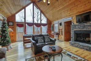 A cozy cabin interior with a fireplace, leather sofa, and a Christmas tree.
