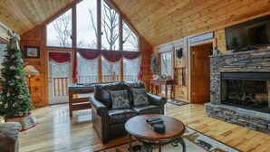 A cozy cabin interior with a fireplace, leather sofa, and a Christmas tree.