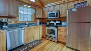 A kitchen with wooden cabinets, stainless steel appliances, and a window with blinds.