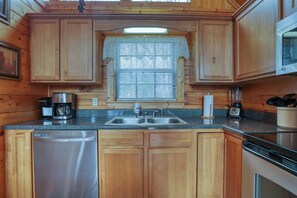 Una cocina con armarios de madera, lavavajillas de acero inoxidable, pileta doble y microondas.