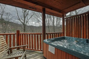 Una terraza de madera con un jacuzzi, un banco de madera y vistas a árboles y colinas.