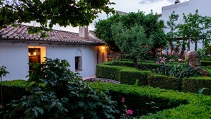 A well-maintained garden with hedges, a stone bridge, and a white building with a tiled roof.