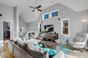 Ein geräumiges Wohnzimmer mit einem modernen Sofa, einem Fernseher und einem Deckenventilator.