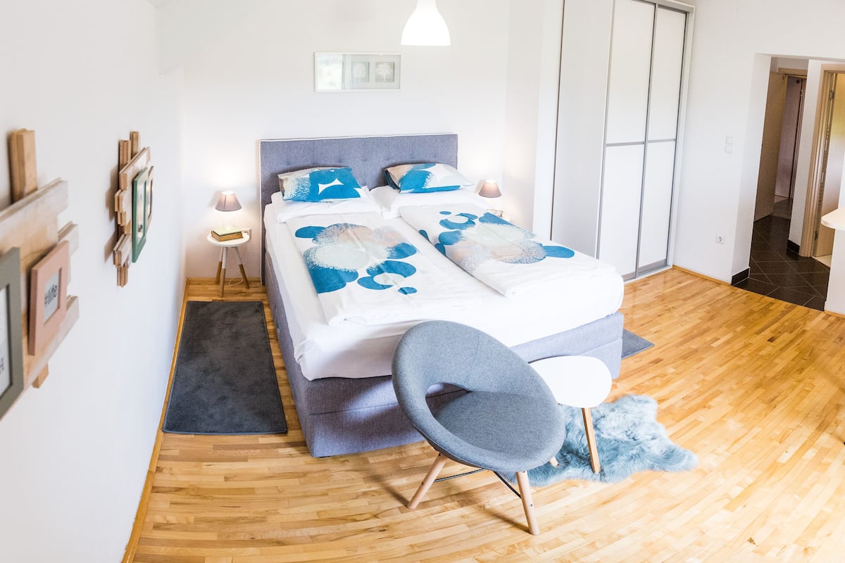 Een slaapkamer met een bed, nachtkastjes, een stoel, een garderobe en een deur.