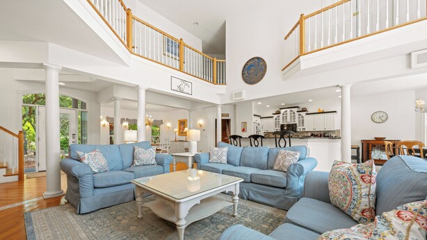 A spacious living area with a large sectional sofa, a coffee table, and a patterned rug. A staircase with wooden railings leads to an upper level.