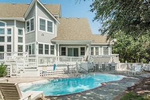 A pool area with a pool, lounge chairs, and a building with a porch.