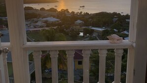 A balcony with a view of a sunset over the sea, a white railing, and a shell on the balustrade.
