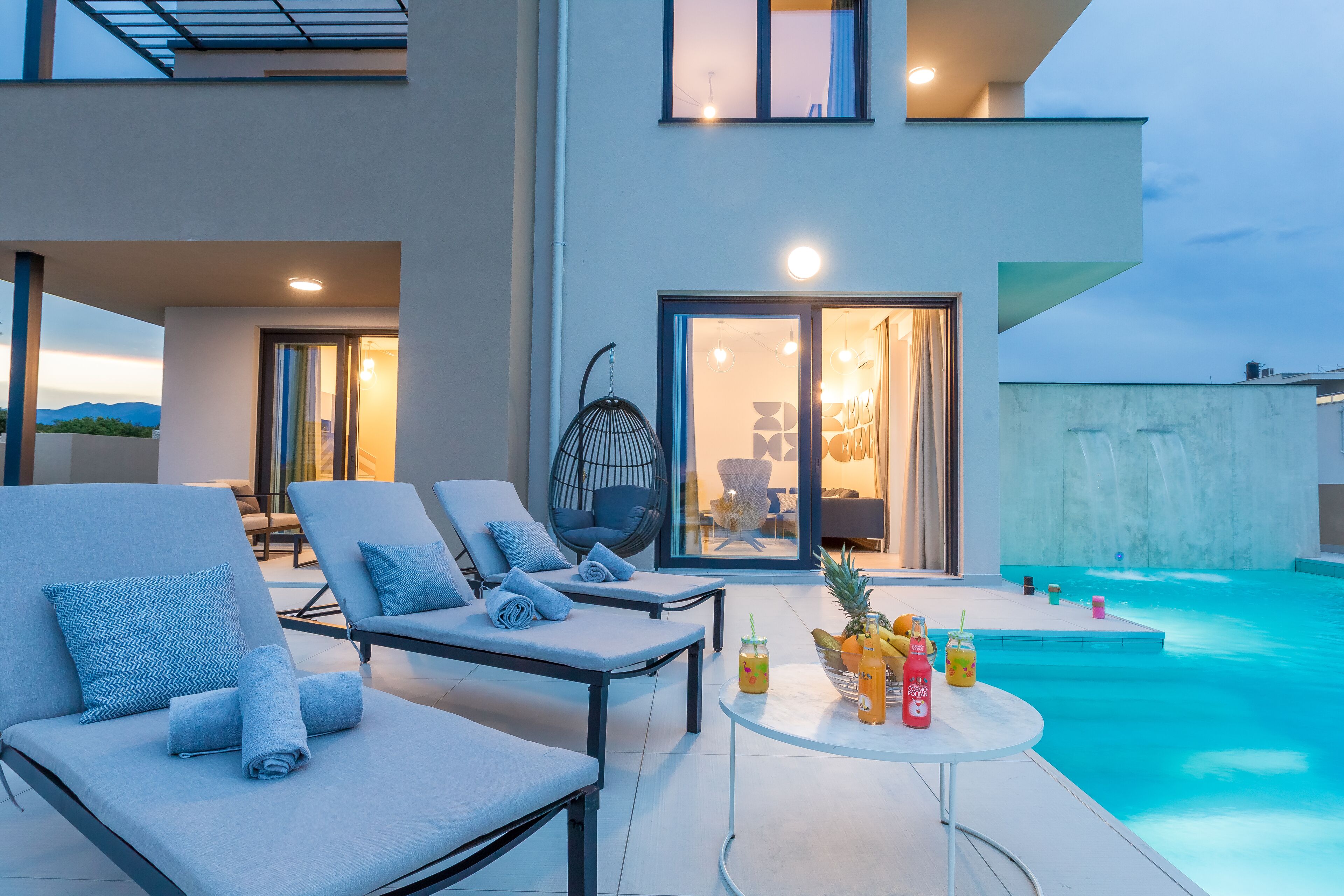 Un área de piscina moderna al aire libre con sillones de descanso y una mesa con bebidas.