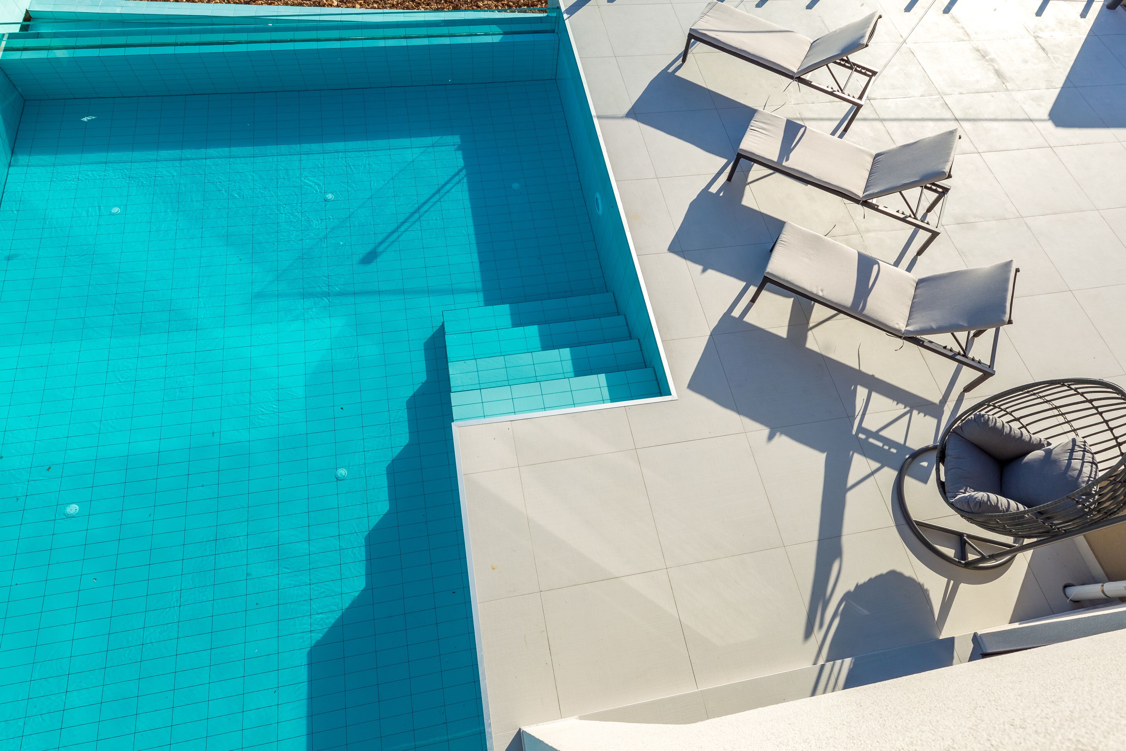 Une piscine sur le toit, bordée de carreaux, un ensemble de chaises d’extérieur et un fauteuil suspendu.
