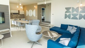A modern living room with a blue sofa, a round coffee table, and a dining area with chairs and a table. - Villa Sara (Novalja)