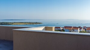 A coastal view from a balcony with a clear sky, a distant island, and a row of houses with red roofs. - Villa Sara (Novalja)