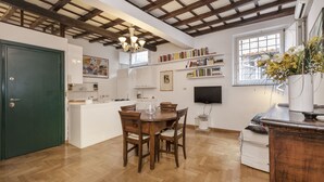 A dining area with a wooden table and chairs, a green door, and a bookshelf with books.