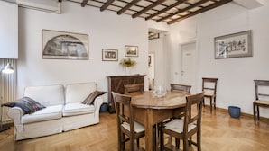 A dining area with a wooden table and chairs, a white sofa with cushions, and framed pictures on the walls.