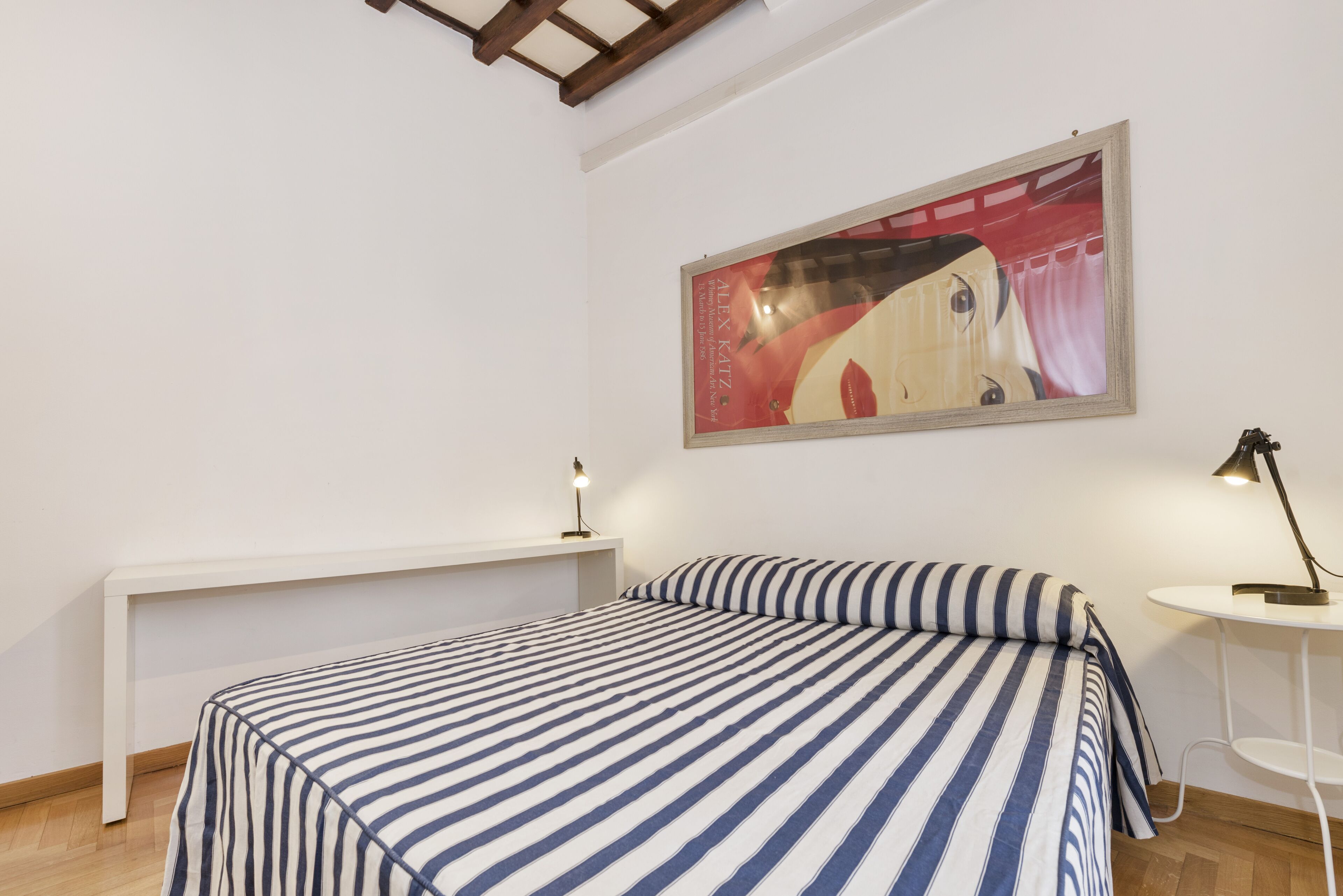 A bedroom with a bed, a bench, a small table, and a painting on the wall.