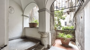 A narrow corridor with stone steps leading to a balcony, flanked by white walls and columns.