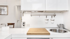 A modern kitchen with white cabinets, a wooden cutting board, a stainless steel sink, and a hanging pot rack.