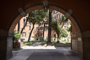 Un corredor arqueado con vistas a un patio, donde se aprecia un árbol y un edificio con múltiples ventanas.