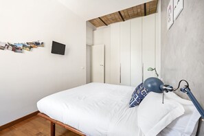 Un dormitorio con una cama, una lámpara de escritorio y un televisor montado en la pared.