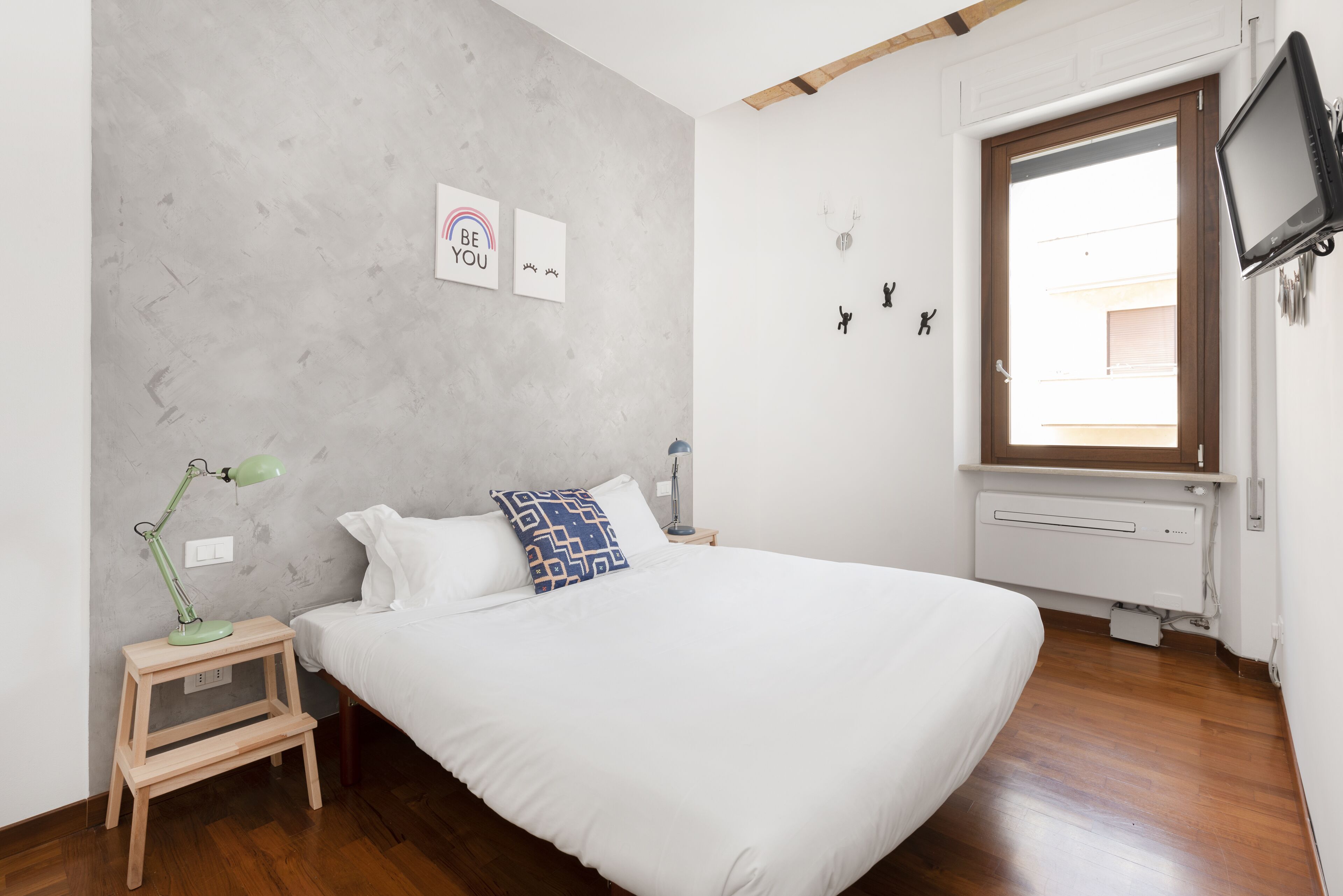 Un dormitorio con cama, mesita de noche, lámpara, ventana y pared decorada con mensajes motivacionales.