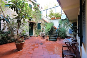 A courtyard with terracotta tiles, potted plants, a wooden bench, a table, and a staircase. - Palline (Rome)