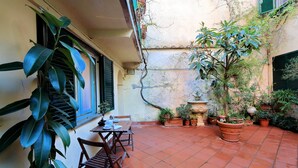 Un patio con suelo de baldosas, una mesa con sillas, plantas en macetas y una fuente.