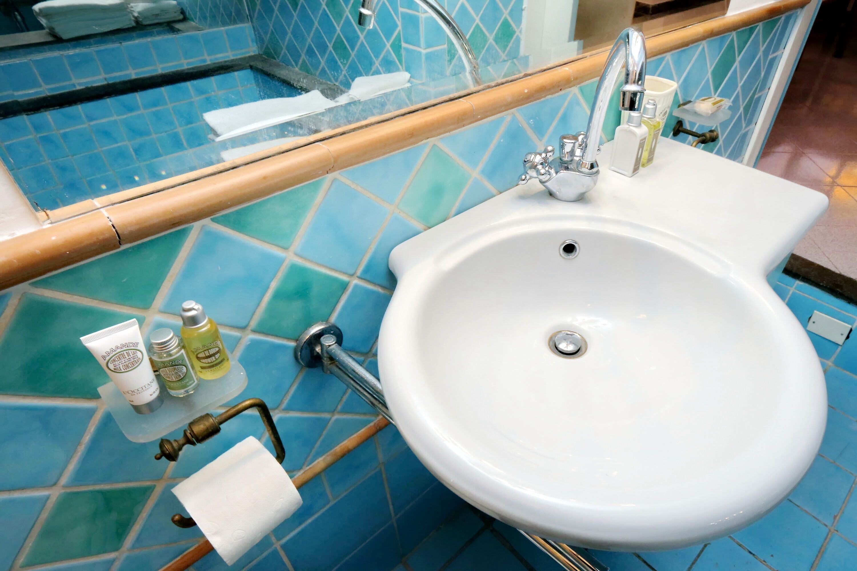 A bathroom with a white sink, blue tiles, and toiletries on the counter.