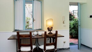 Un comedor con una mesa y sillas, una ventana con cortinas, una lámpara de mesa y vistas de un jardín a través de una puerta abierta.