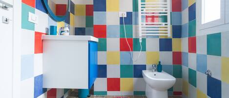 Un baño con azulejos coloridos, un lavamanos blanco, un bidé y una alfombra circular en el suelo.