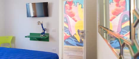 A room with a bed, a TV mounted on the wall, a green shelf, and a colorful mural on the door.
