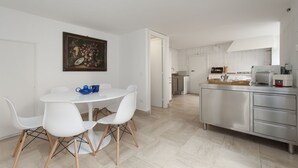 Een moderne keuken met witte kastjes, een roestvrijstalen aanrecht en een eethoek met een witte tafel en stoelen.