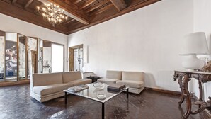 Een ruime woonkamer met een hoge plafond, een glazen salontafel, twee banken en een houten tafel met een lamp.